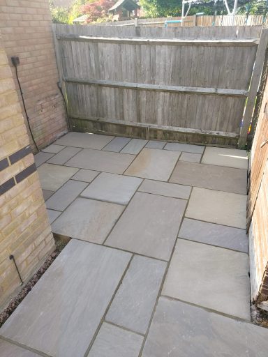 Paved outdoor area with rectangular stone slabs and a wooden fence backdrop.