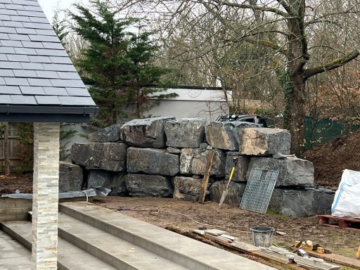 Piled large stones beside a building, with a few construction materials visible.